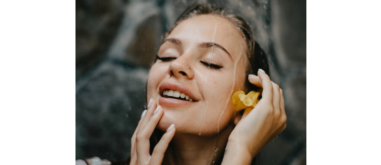 Happy woman feeling water on face during refreshing hair rinse.